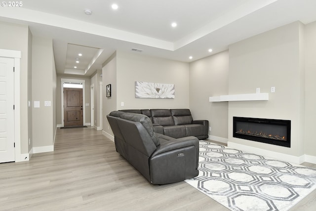 living room with a raised ceiling, recessed lighting, baseboards, and light wood finished floors