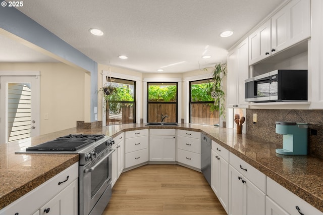 kitchen with appliances with stainless steel finishes, tile counters, white cabinetry, light wood-type flooring, and recessed lighting