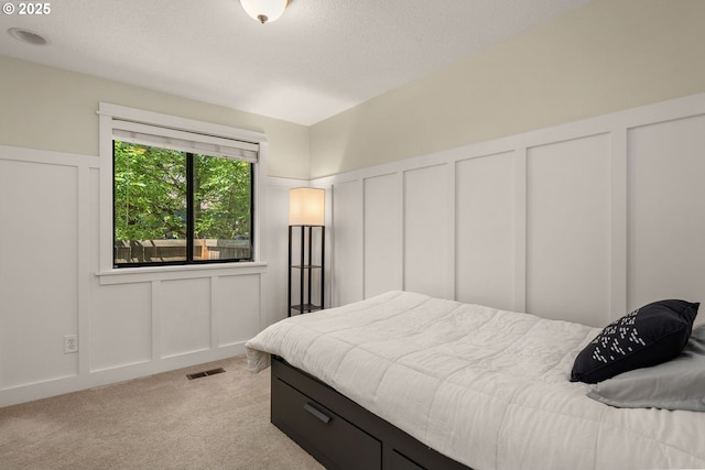 bedroom with a decorative wall, light colored carpet, a wainscoted wall, and a textured ceiling