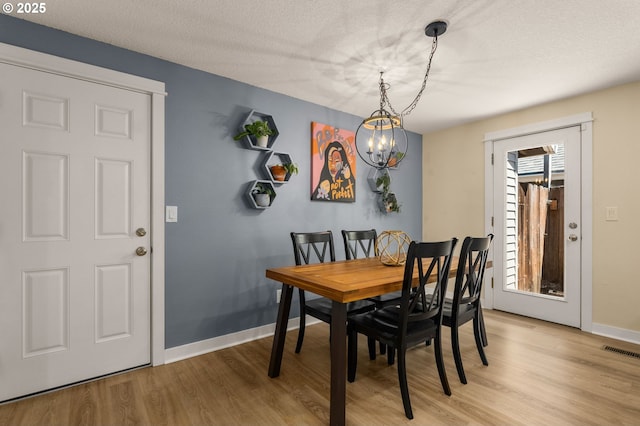 dining room featuring a chandelier, light wood-type flooring, baseboards, and a textured ceiling