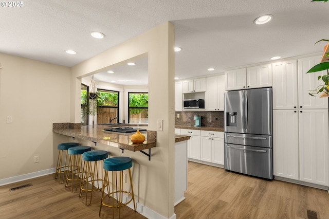 kitchen featuring appliances with stainless steel finishes, light wood-type flooring, a kitchen bar, backsplash, and white cabinets