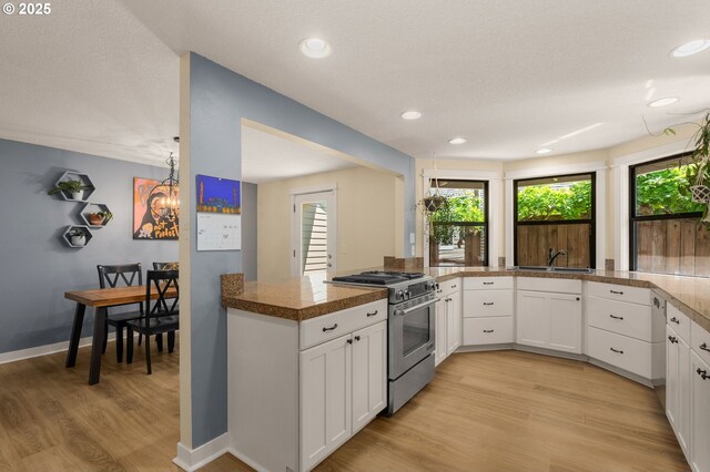 kitchen with high end stainless steel range, light wood-type flooring, a sink, white cabinetry, and recessed lighting