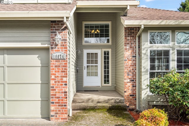 property entrance featuring an attached garage, brick siding, and a shingled roof