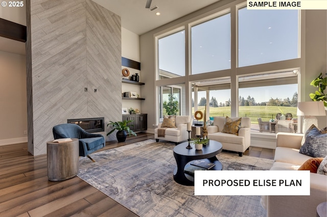 living room with a tile fireplace, a towering ceiling, baseboards, and wood finished floors