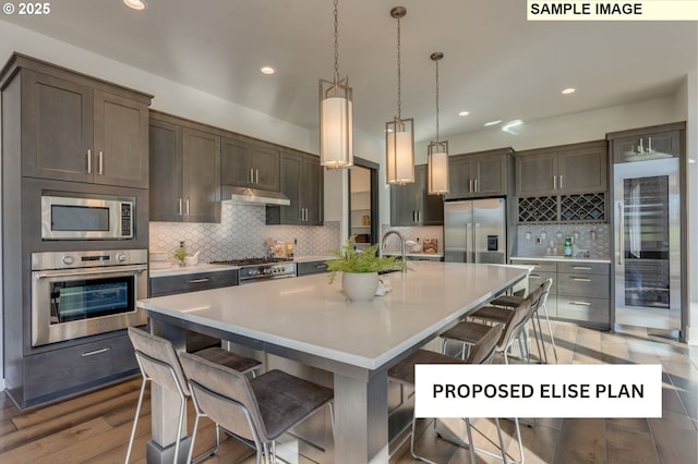 kitchen featuring appliances with stainless steel finishes, a breakfast bar, under cabinet range hood, and tasteful backsplash