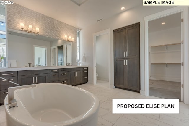 bathroom featuring marble finish floor, recessed lighting, toilet, vanity, and a freestanding tub