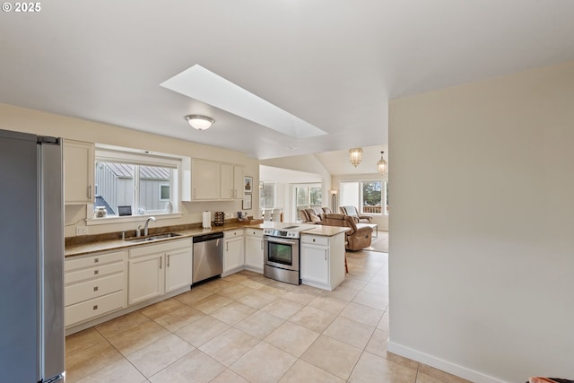 kitchen featuring vaulted ceiling with skylight, sink, light tile patterned floors, kitchen peninsula, and stainless steel appliances