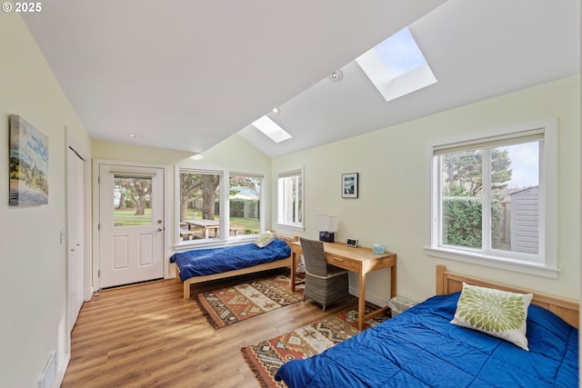 bedroom with lofted ceiling with skylight and light hardwood / wood-style flooring