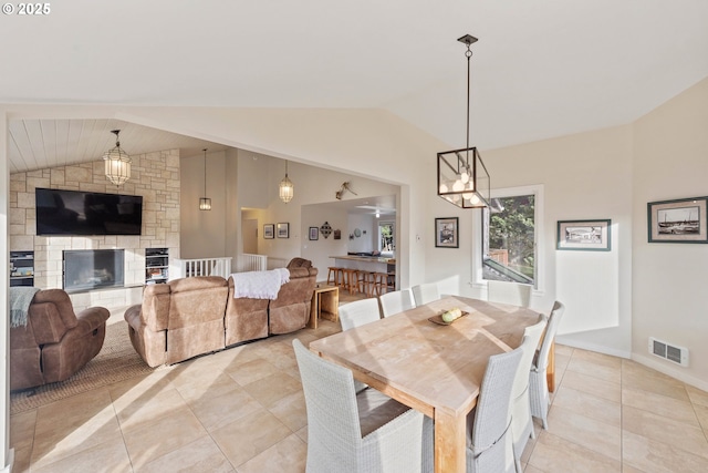 dining space with lofted ceiling, light tile patterned floors, and a stone fireplace