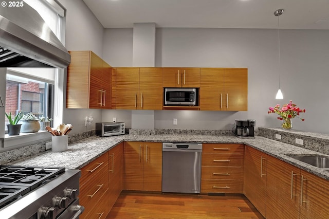 1746 NW Riverscape St, Portland, OR 97209 - kitchen featuring stainless steel appliances, light wood-style floors, wall chimney exhaust hood, and brown cabinetry