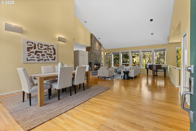 dining area featuring light hardwood / wood-style floors, high vaulted ceiling, and a fireplace