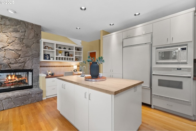 kitchen with built in appliances, a kitchen island, a stone fireplace, and white cabinets