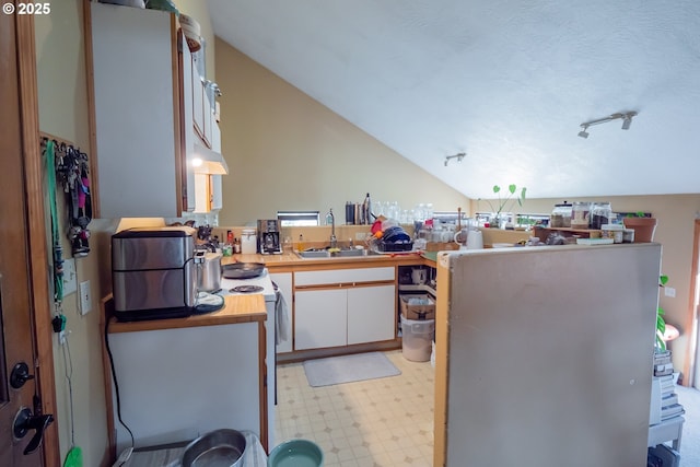 kitchen featuring sink, white cabinetry, vaulted ceiling, a textured ceiling, and kitchen peninsula