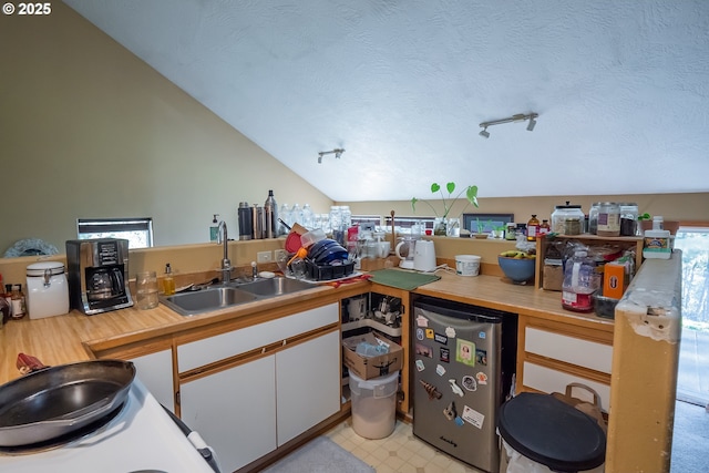 kitchen with lofted ceiling, sink, white cabinetry, a textured ceiling, and stainless steel fridge