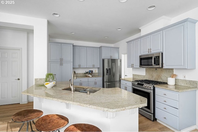 kitchen with appliances with stainless steel finishes, a breakfast bar area, a sink, and light stone counters