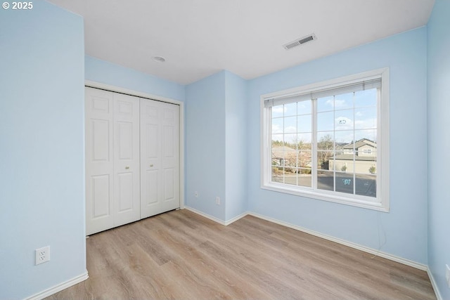 unfurnished bedroom featuring baseboards, a closet, visible vents, and wood finished floors