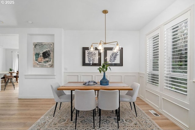 dining area with light wood finished floors, an inviting chandelier, visible vents, and a decorative wall