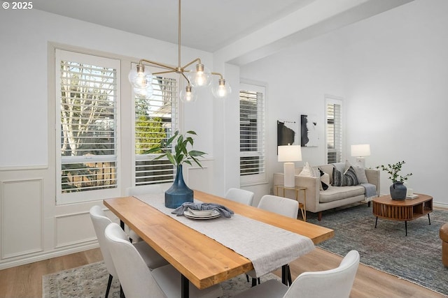 dining area with light wood finished floors, a decorative wall, and an inviting chandelier