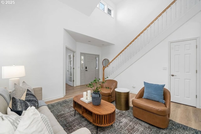 living area featuring baseboards, stairway, a towering ceiling, and wood finished floors