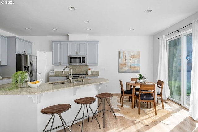 kitchen featuring light wood-style flooring, stainless steel appliances, a breakfast bar, a sink, and light stone countertops