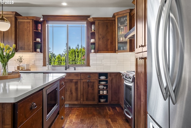 kitchen with stainless steel appliances, open shelves, a sink, dark wood finished floors, and tasteful backsplash