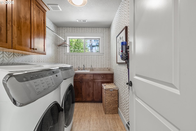 washroom with washer and clothes dryer, cabinet space, wallpapered walls, and a textured ceiling