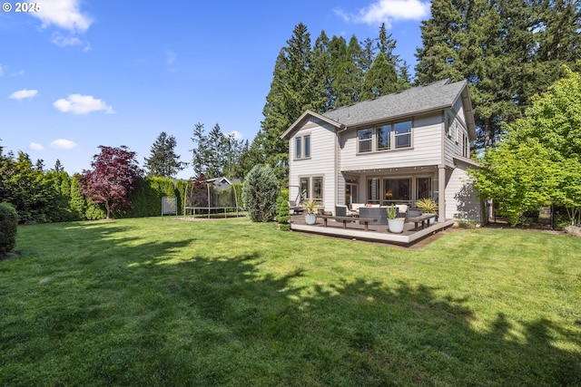 rear view of house featuring a trampoline, an outdoor living space, a lawn, and a wooden deck