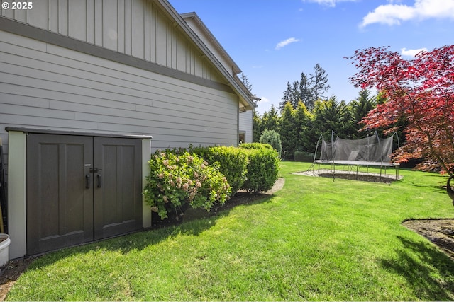 view of green lawn featuring a trampoline, a storage unit, and an outdoor structure