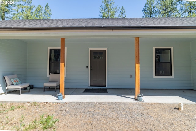 view of exterior entry with a patio and a shingled roof