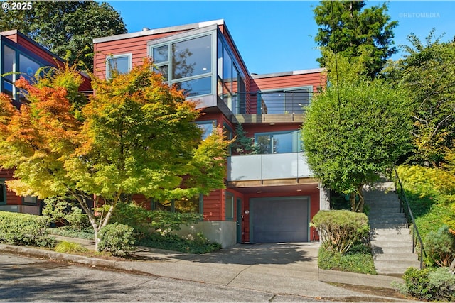 view of front of property featuring stairway, an attached garage, a balcony, and driveway