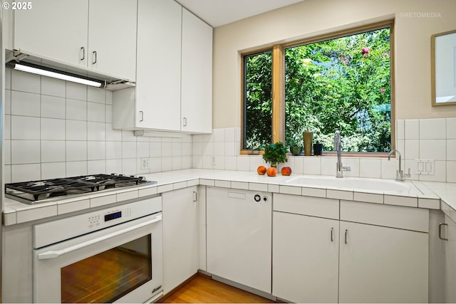kitchen featuring oven, stainless steel gas stovetop, a sink, tile counters, and tasteful backsplash
