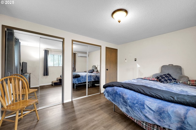 bedroom featuring multiple closets, wood finished floors, a wall mounted air conditioner, a textured ceiling, and baseboards