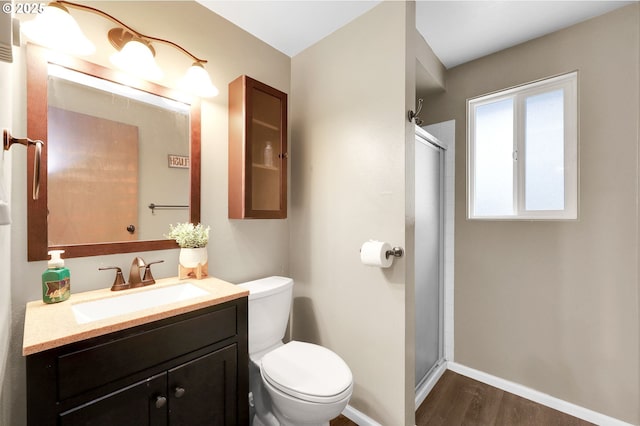 bathroom with toilet, a shower stall, wood finished floors, vanity, and baseboards