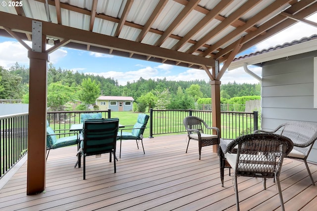 deck featuring an outbuilding, outdoor dining space, and a forest view