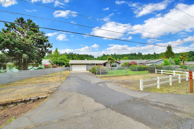 ranch-style house with driveway, a fenced front yard, an attached garage, and view of scattered trees