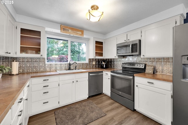 kitchen featuring stainless steel appliances, a sink, white cabinets, decorative backsplash, and a textured ceiling