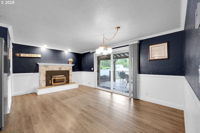 unfurnished living room featuring crown molding, wainscoting, a textured ceiling, a chandelier, and wood finished floors
