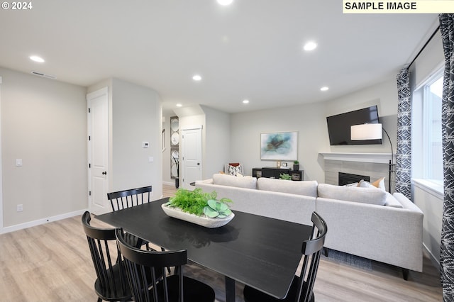 dining space with a tiled fireplace and light hardwood / wood-style flooring