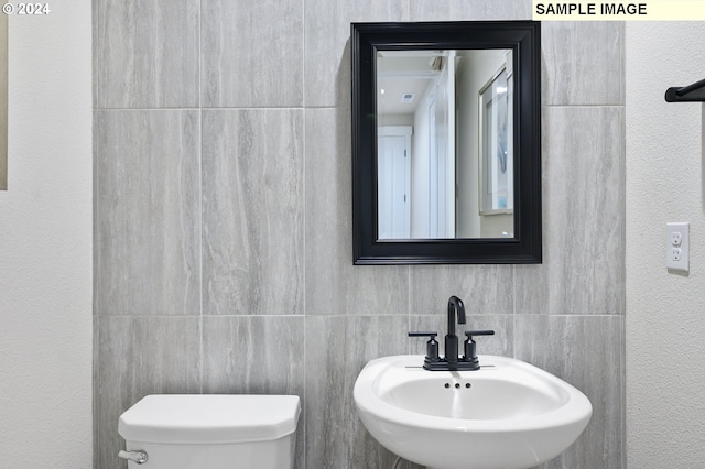 bathroom with toilet, sink, and tile walls