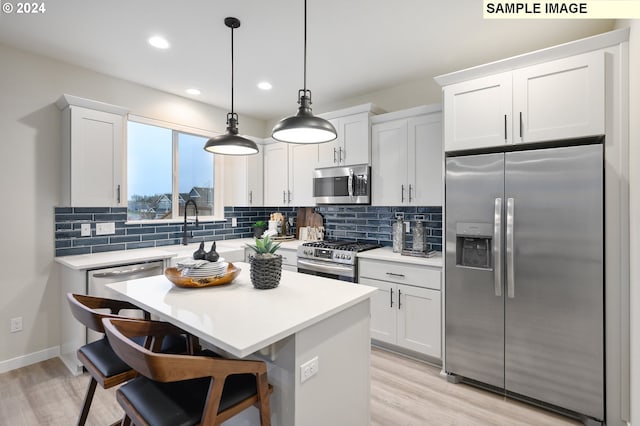 kitchen with pendant lighting, a breakfast bar, appliances with stainless steel finishes, white cabinets, and a kitchen island