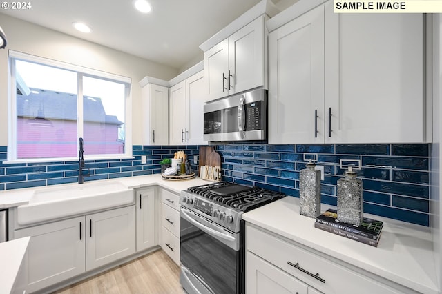 kitchen with appliances with stainless steel finishes, sink, backsplash, white cabinets, and light wood-type flooring