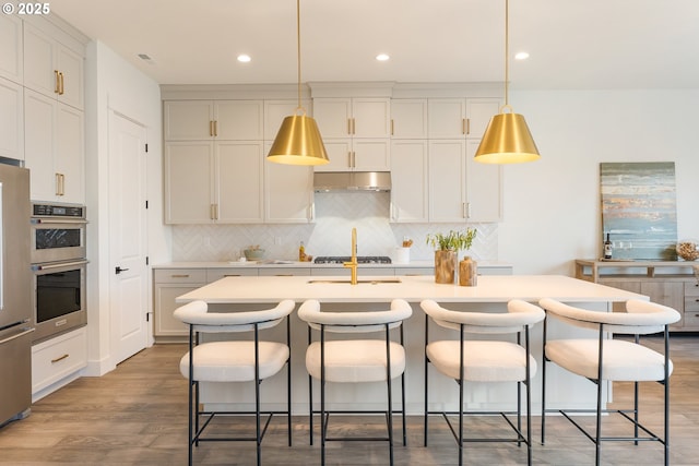 kitchen with a breakfast bar, decorative light fixtures, an island with sink, wood-type flooring, and stainless steel appliances