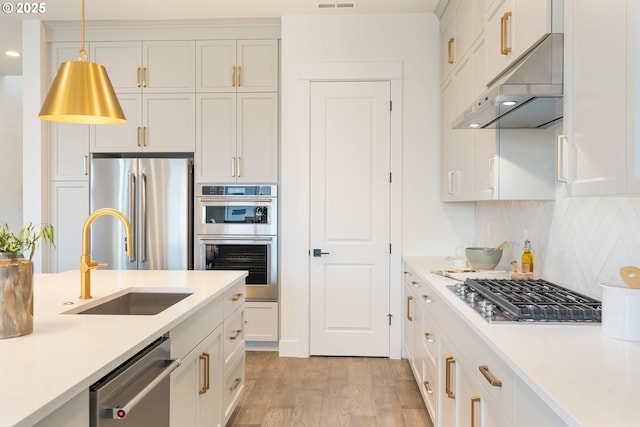 kitchen with light wood-type flooring, under cabinet range hood, a sink, appliances with stainless steel finishes, and light countertops