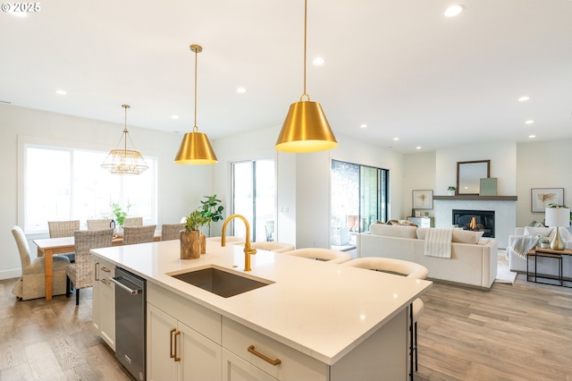 kitchen with sink, light hardwood / wood-style flooring, hanging light fixtures, an island with sink, and white cabinets