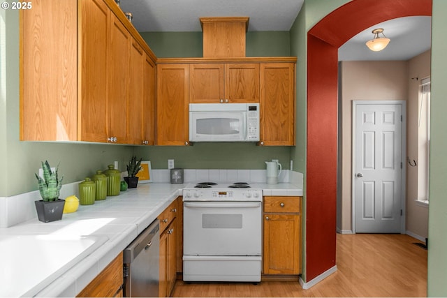 6073 SW 205th Ave, Beaverton, OR 97078 - kitchen featuring white appliances, light wood-style floors, arched walkways, and brown cabinetry