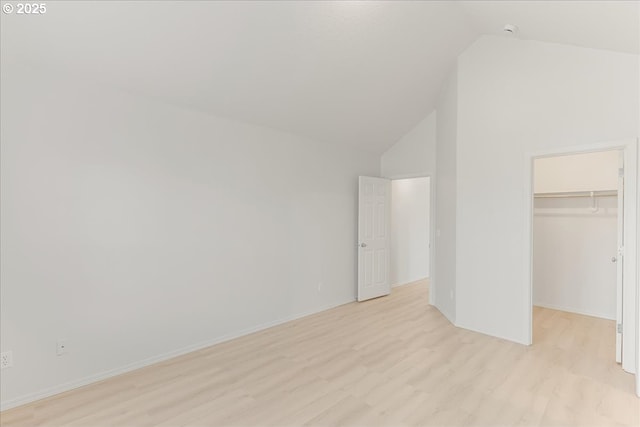 unfurnished bedroom with a walk in closet, light hardwood / wood-style floors, a closet, and vaulted ceiling