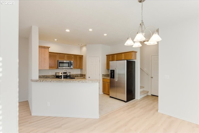 kitchen with appliances with stainless steel finishes, decorative light fixtures, light stone counters, kitchen peninsula, and light hardwood / wood-style flooring