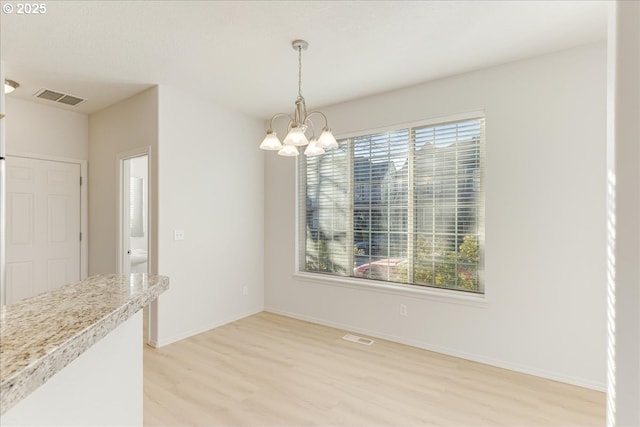 unfurnished dining area featuring an inviting chandelier and light hardwood / wood-style flooring