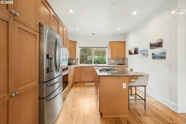 kitchen with a center island, a breakfast bar, decorative backsplash, light wood-style floors, and stainless steel appliances