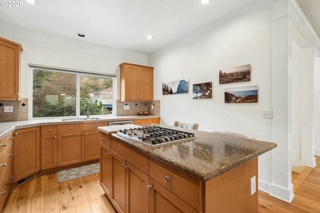 kitchen featuring stainless steel gas cooktop, light wood-type flooring, decorative backsplash, stone counters, and a sink